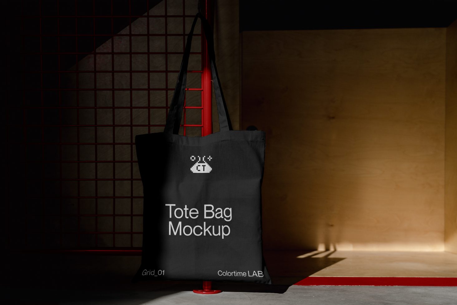 Black tote bag mockup hanging against a textured background with striking lighting, showcasing design and typography space.